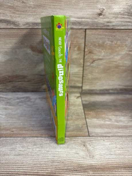 Side view of Never Touch the Dinosaurs board book showing green spine with white title text dinosaurs on wood background