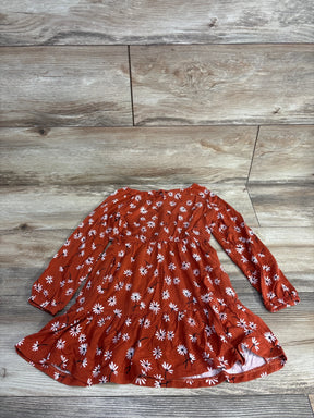 Rust orange long-sleeve toddler dress with white daisy flower pattern on wood floor