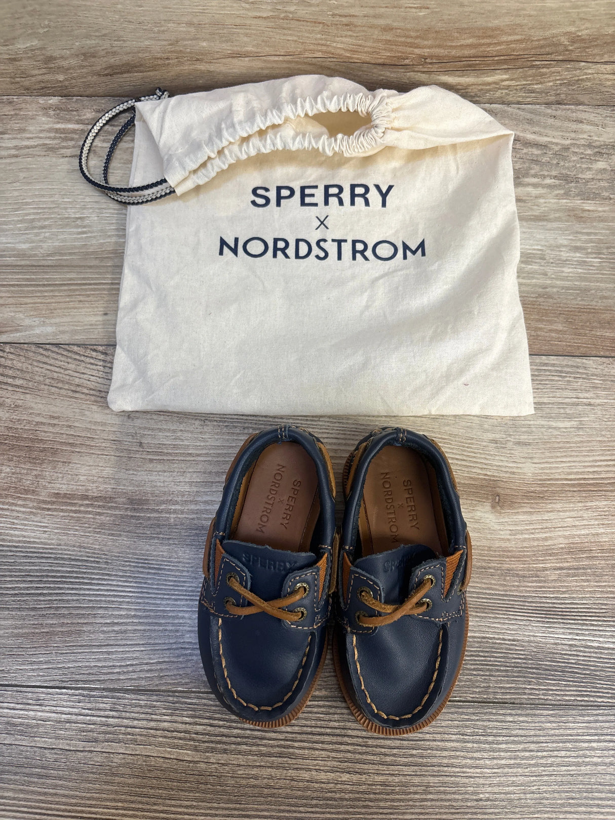 Kids navy blue Sperry x Nordstrom boat shoes with drawstring storage bag on wood floor