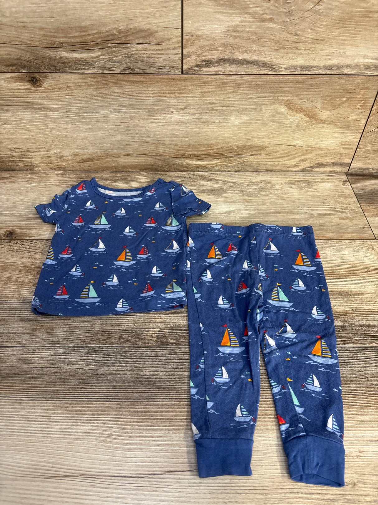 Flat lay of Little Me 2-piece bamboo baby pajama set showcasing multicolored sailboat print on blue fabric with wooden background