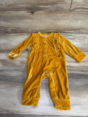 Yellow velvet baby romper with long sleeves, ruffle details, and buttons on wood floor