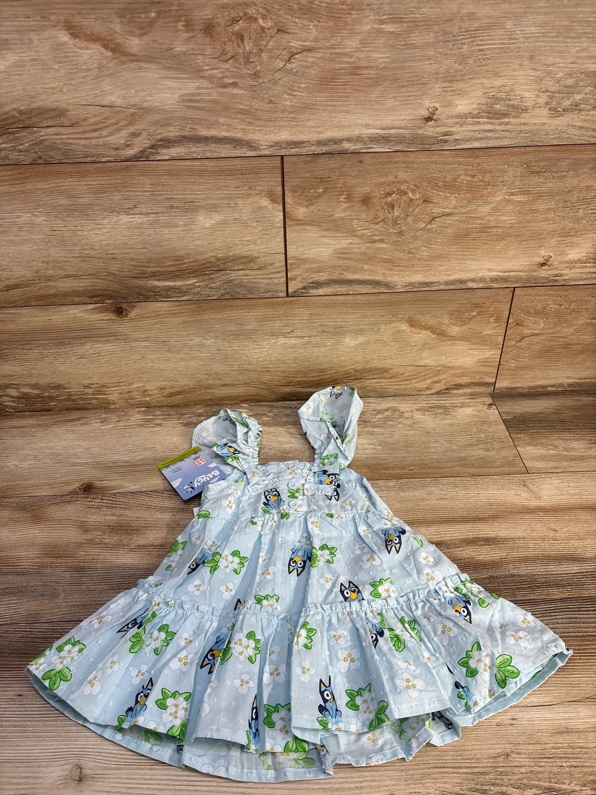 Flat lay of light blue 12M toddler dress with Swiss-dot, ruffled straps, tiered skirt and Bluey floral print on wood