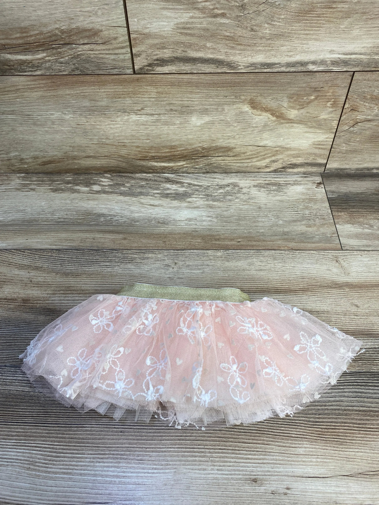 Flat lay of pink embroidered tulle baby skirt size 0-12 months showcasing gold elastic waistband on wood background
