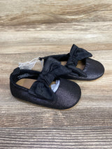 Pair of black glitter baby shoes with large black bows, displayed on wooden surface