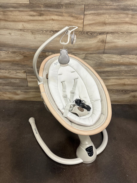 Top view of Maxi-Cosi Cassia baby swing in Classic Oat showing padded seat, toy bar, and control panel on wood flooring