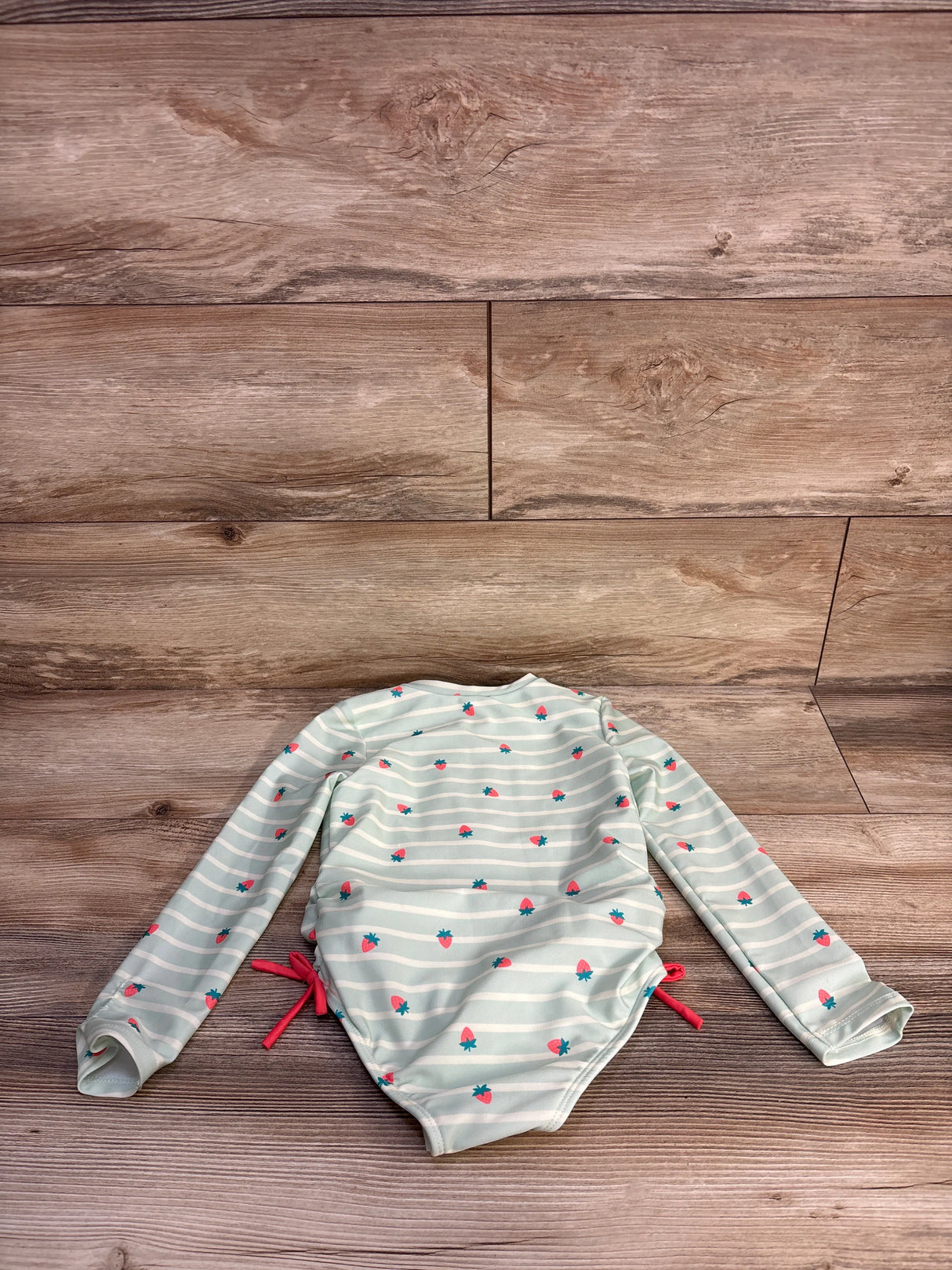 Flat lay of Cat and Jack girls' long-sleeve striped rash guard with strawberry print and side ties on wood background