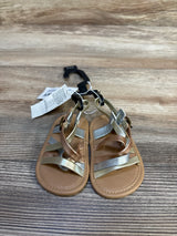 Infant brown and silver strappy sandals with tags on a wood surface