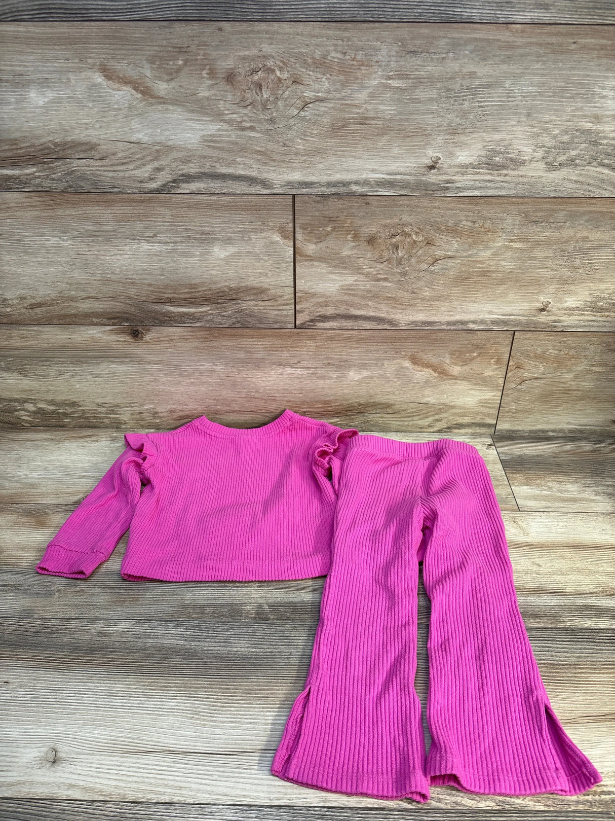 Bright pink ribbed kids outfit with ruffle top and flared pants on wood floor