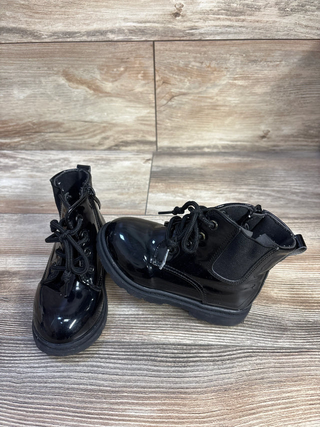 Side front view of kids' black faux leather lace up boots with glossy finish and chunky sole on wood background