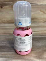 Glass baby bottle with pink silicone sleeve and clear cap on wood background