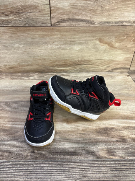 Front three quarter view of black AND1 high-top basketball shoes with red trim, velcro strap and gum sole on wood floor