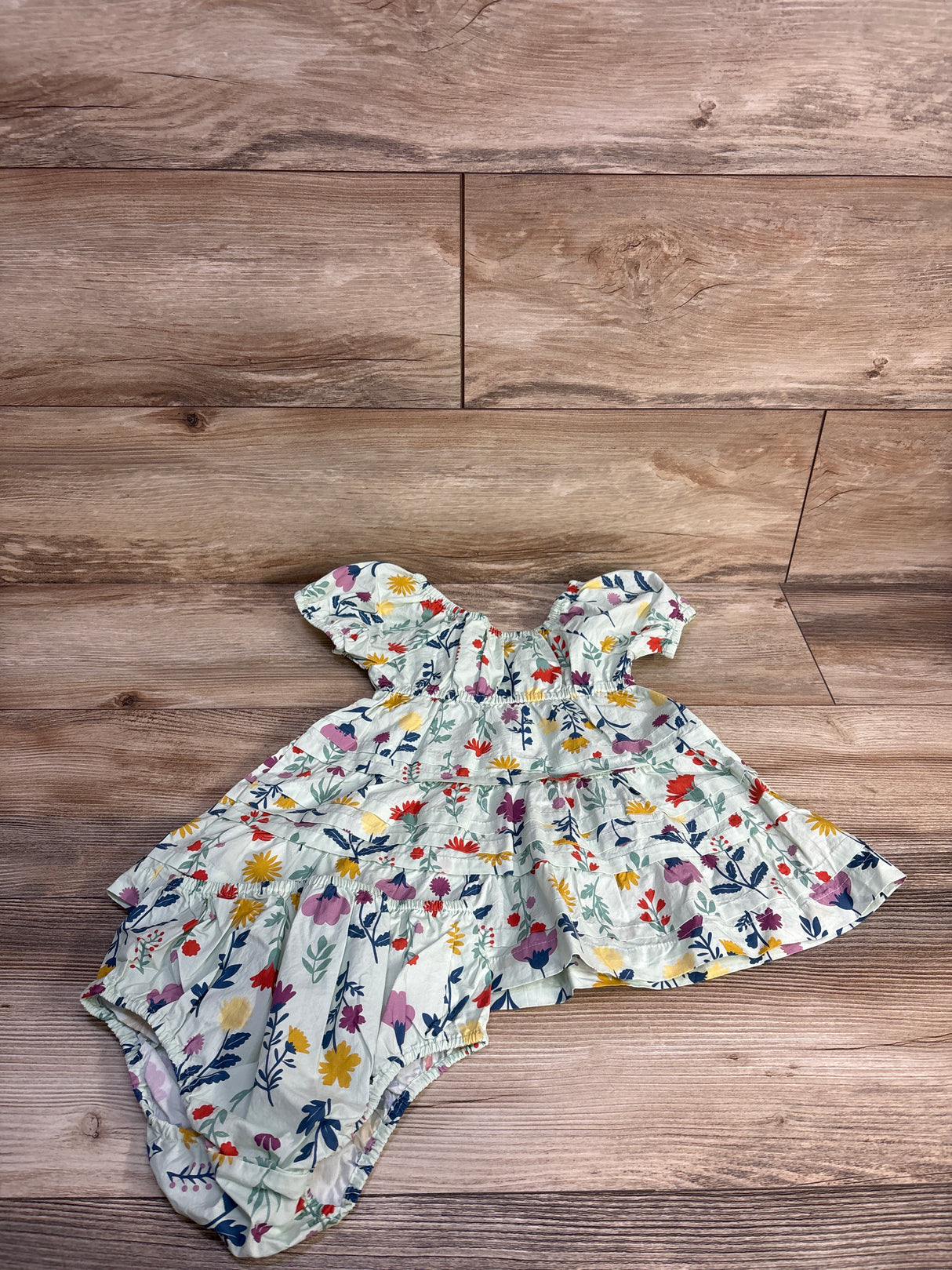 Flat lay of green floral tiered toddler dress with matching bloomers in organic cotton poplin on wood background