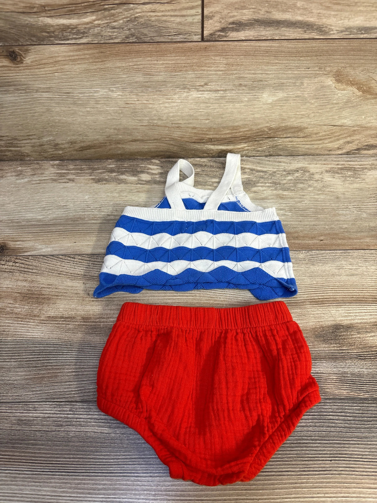 Flat lay of Cat and Jack 2-piece 4th of July set with blue-white tank, white straps, and red bloomers on wood background