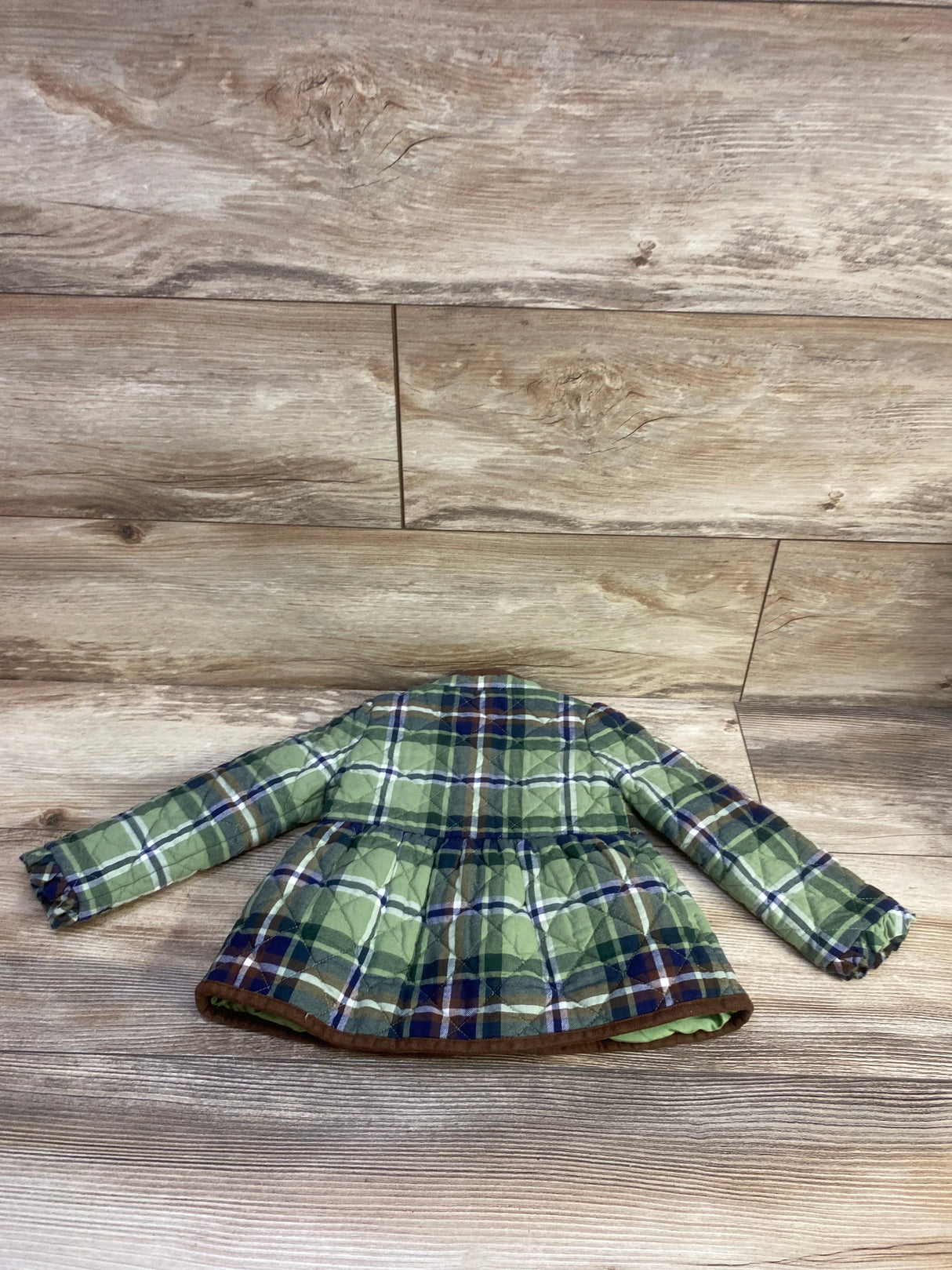Front view of Janie & Jack plaid jacket showcasing green plaid, long sleeves, and flared hem on a wood-look background