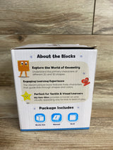 Back view of My Geo-Blox toy box showcasing the 'About the Blocks' text describing learning 2D and 3D shapes and package icons for blocks, manual, book on wood background