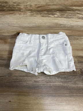 Front view of DL1961 Lucy toddler white denim shorts showing distressed details and frayed hem on wood background