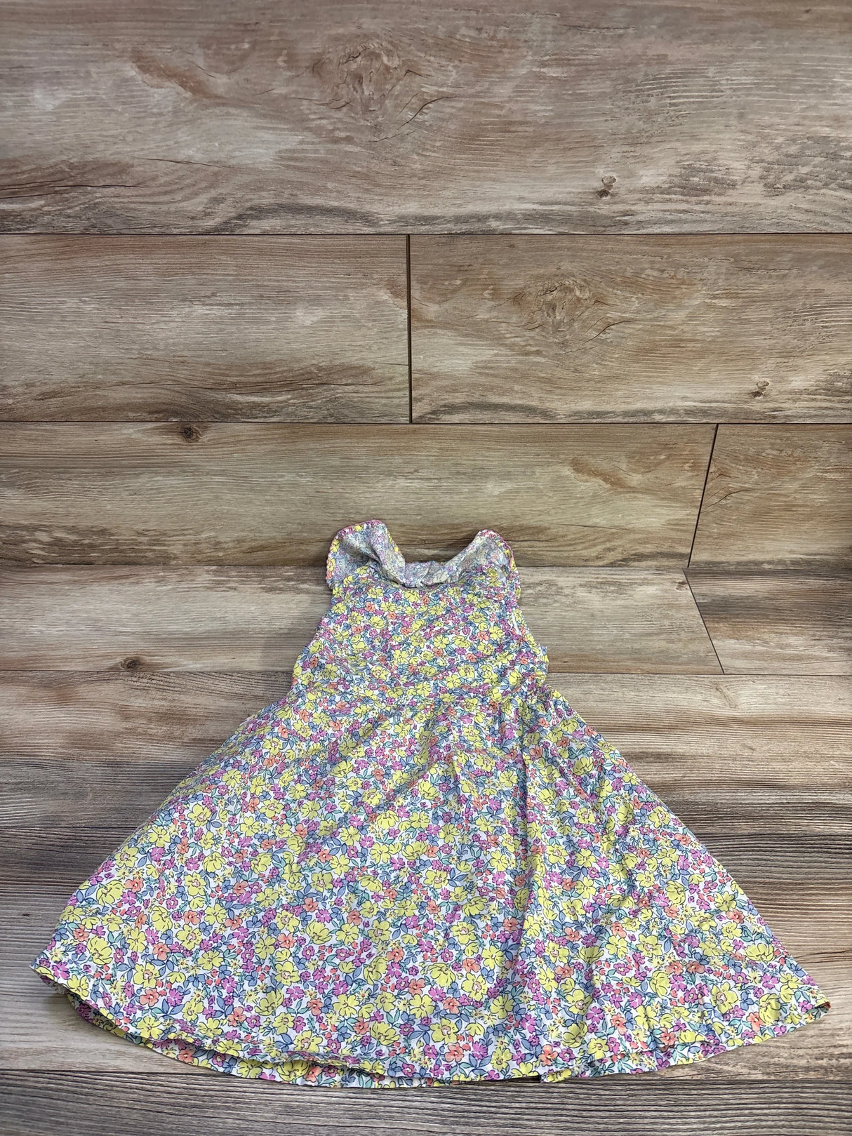 Flat-lay of girls Penelope Mack yellow floral button-front dress showcasing sleeveless ruffled collar and full skirt on wooden floor background