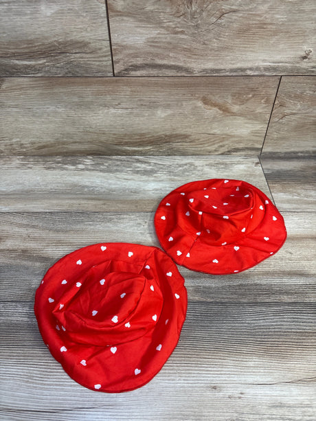 Top-down view of two red heart-print bucket hats showcasing white heart pattern and wide brims on wood floor background