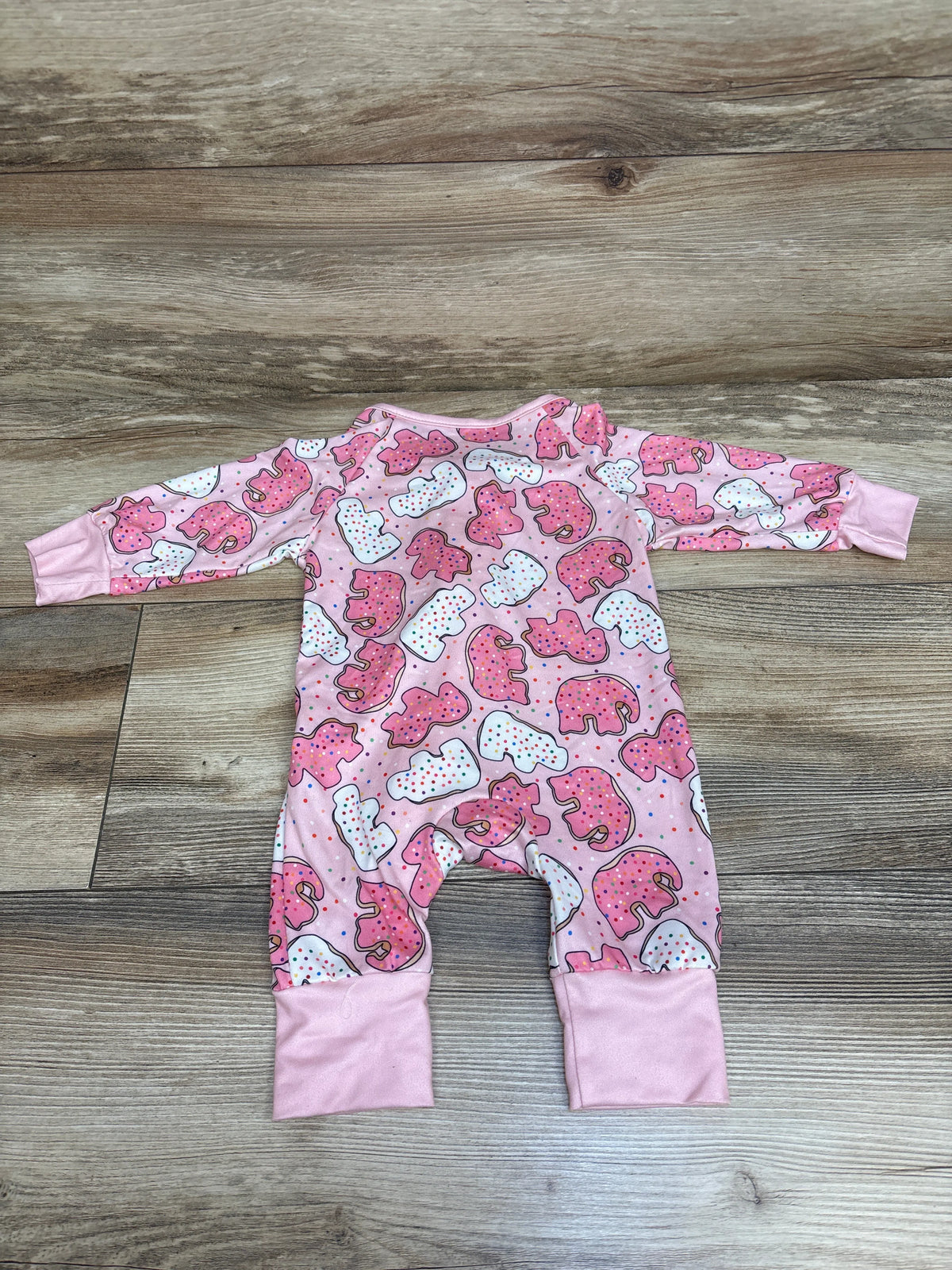 Front view of pink Shein Animal Cracker Sleeper with long sleeves and animal cracker print on a wood background