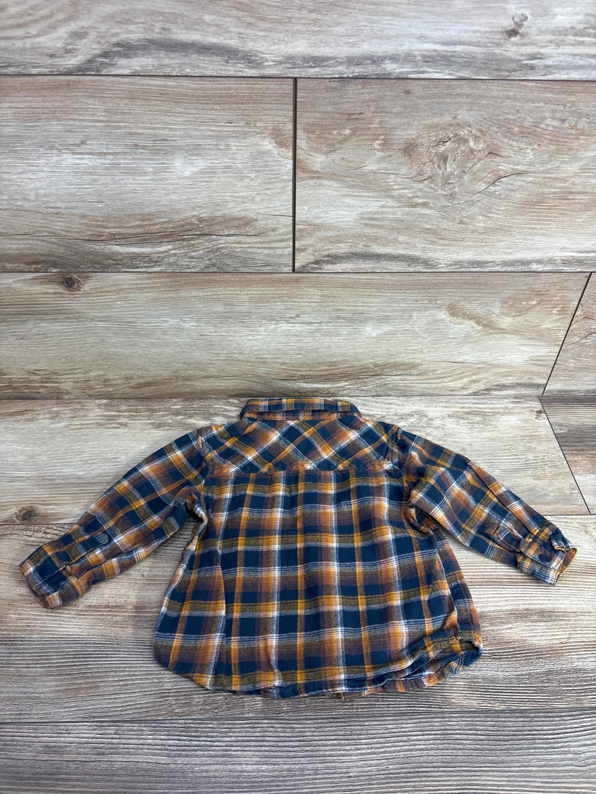 Baby or toddler long-sleeve plaid flannel shirt in navy, orange, and white on wood floor