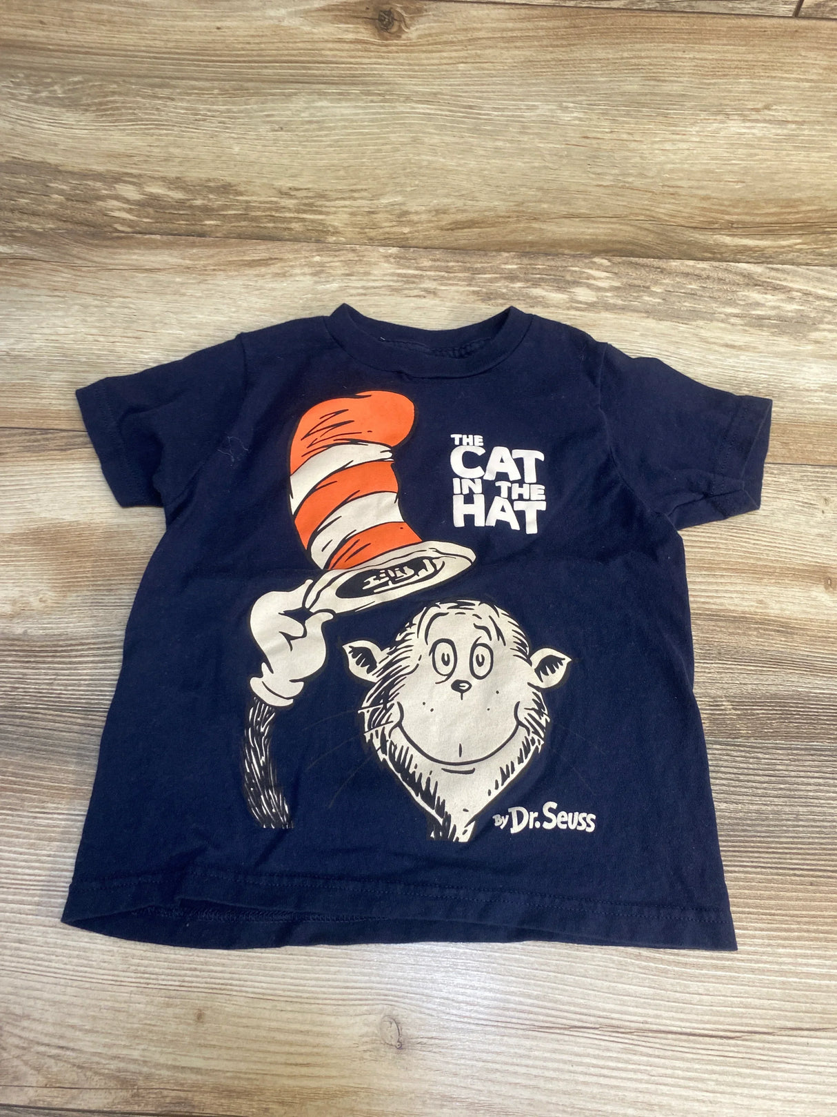 Navy blue kids t-shirt featuring The Cat in the Hat graphic with red striped hat on wood background
