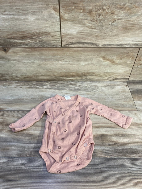 Flat lay of Kate Quinn Organic bodysuit in dusty pink showing wrap-front, long sleeves and snap crotch on wood background