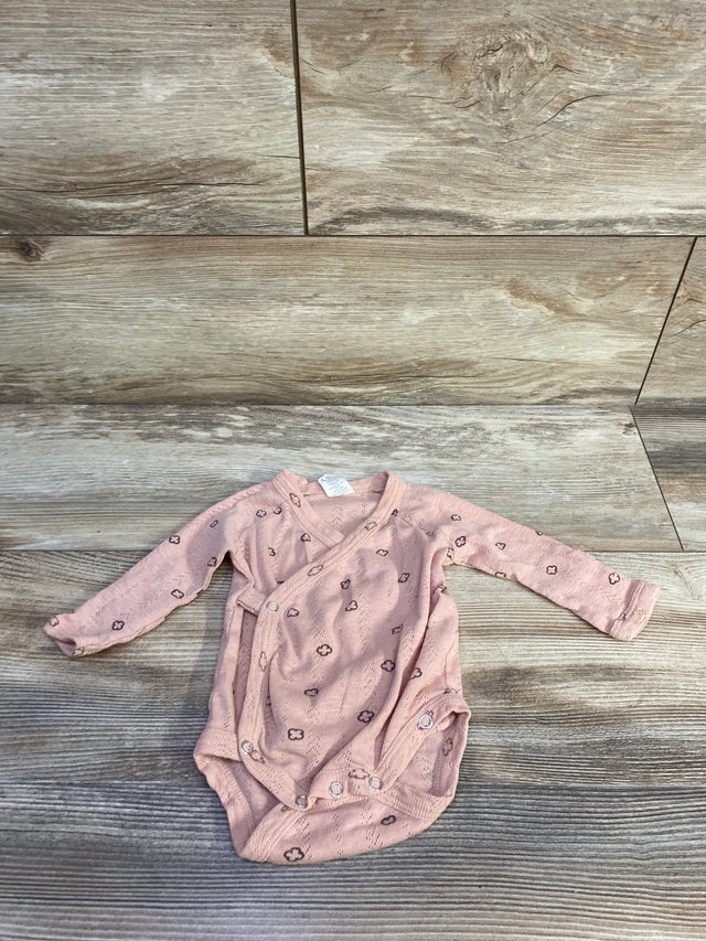 Flat lay of Kate Quinn Organic bodysuit in dusty pink showing wrap-front, long sleeves and snap crotch on wood background
