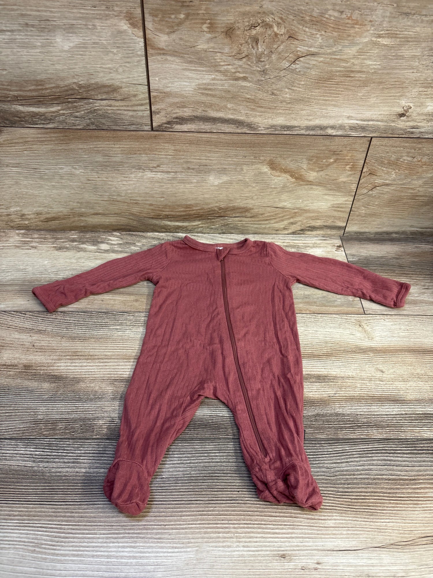 Front view of red ribbed viscose sleeper in newborn size with long sleeves, zipper, and footed legs on wood-look background