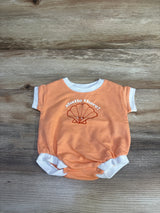 Flat lay of orange newborn terry romper with white ringer trim, shell graphic and "shello there!" text on wood background