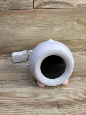 Angled front of LittleHippo Mella Ready To Rise sleep trainer showing black display, pink feet, and power cord on wood