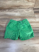 Top-down of green baby drawstring shorts showing elastic waist braided drawstring and front pockets on wood background