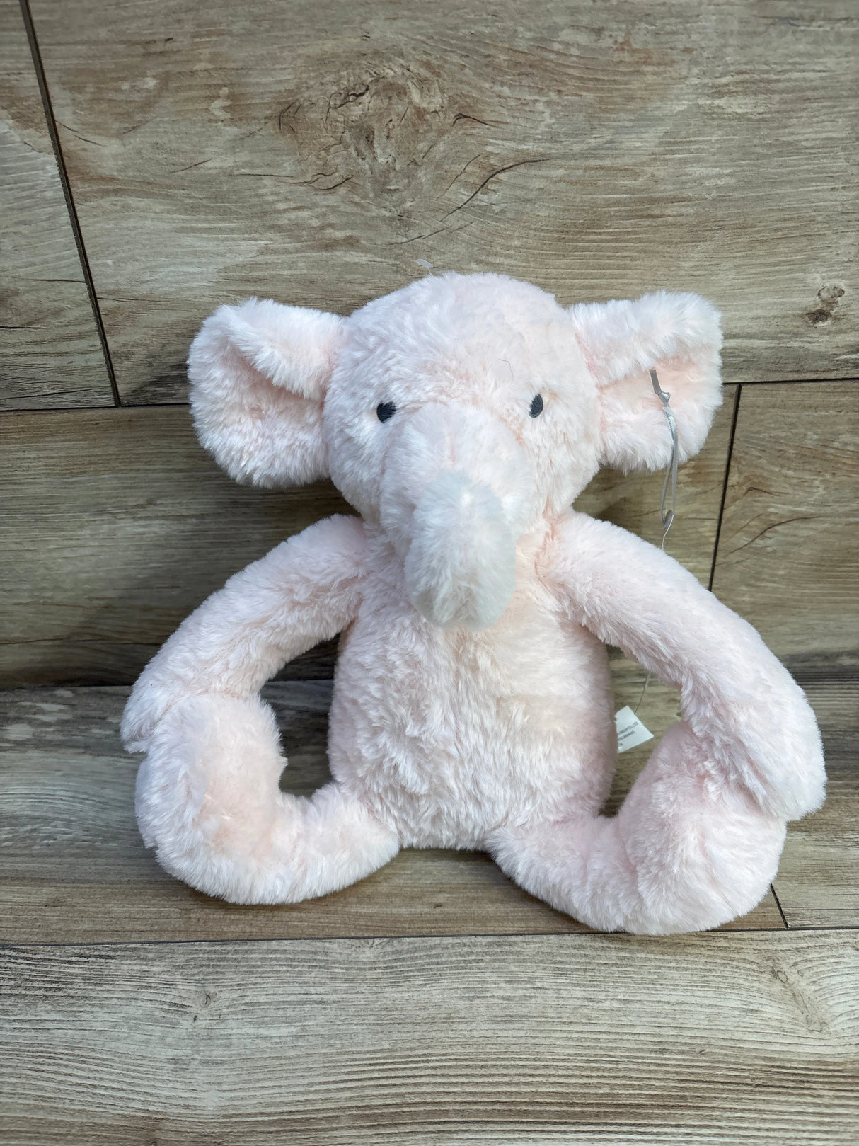 Front view of Cloud Island pink elephant plush showcasing soft fluffy fur and long bendable trunk with wood plank background