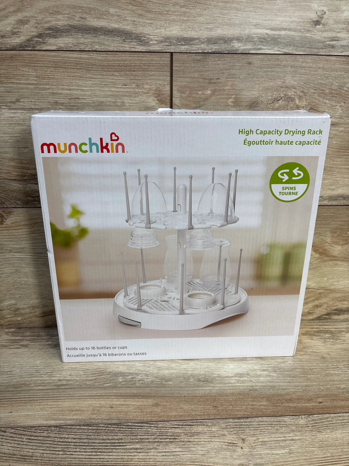 Front view of Munchkin high-capacity bottle drying rack showing dual-tier spinning pegs and drip tray on wooden tabletop background