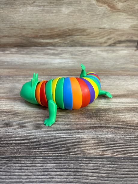 Side view of Ja-Ru sensory fidget axolotl showing rainbow segmented body and green head on a wood tabletop