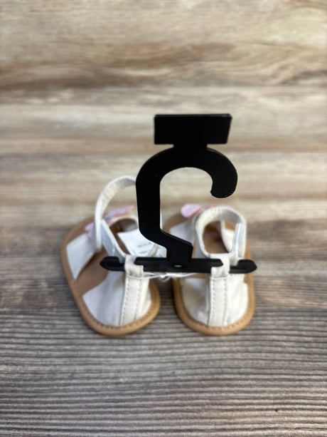 White baby sandals with tan soles on a display hanger, placed on wooden background