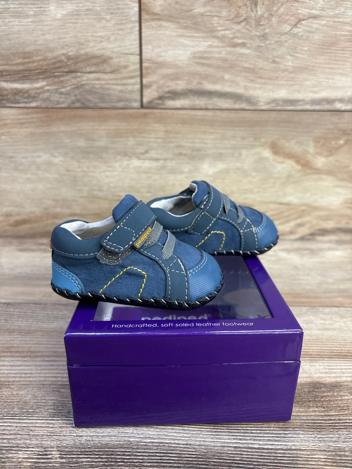 Front-right view of navy Pediped Dani crib shoes showing velcro strap and soft leather upper on a purple box