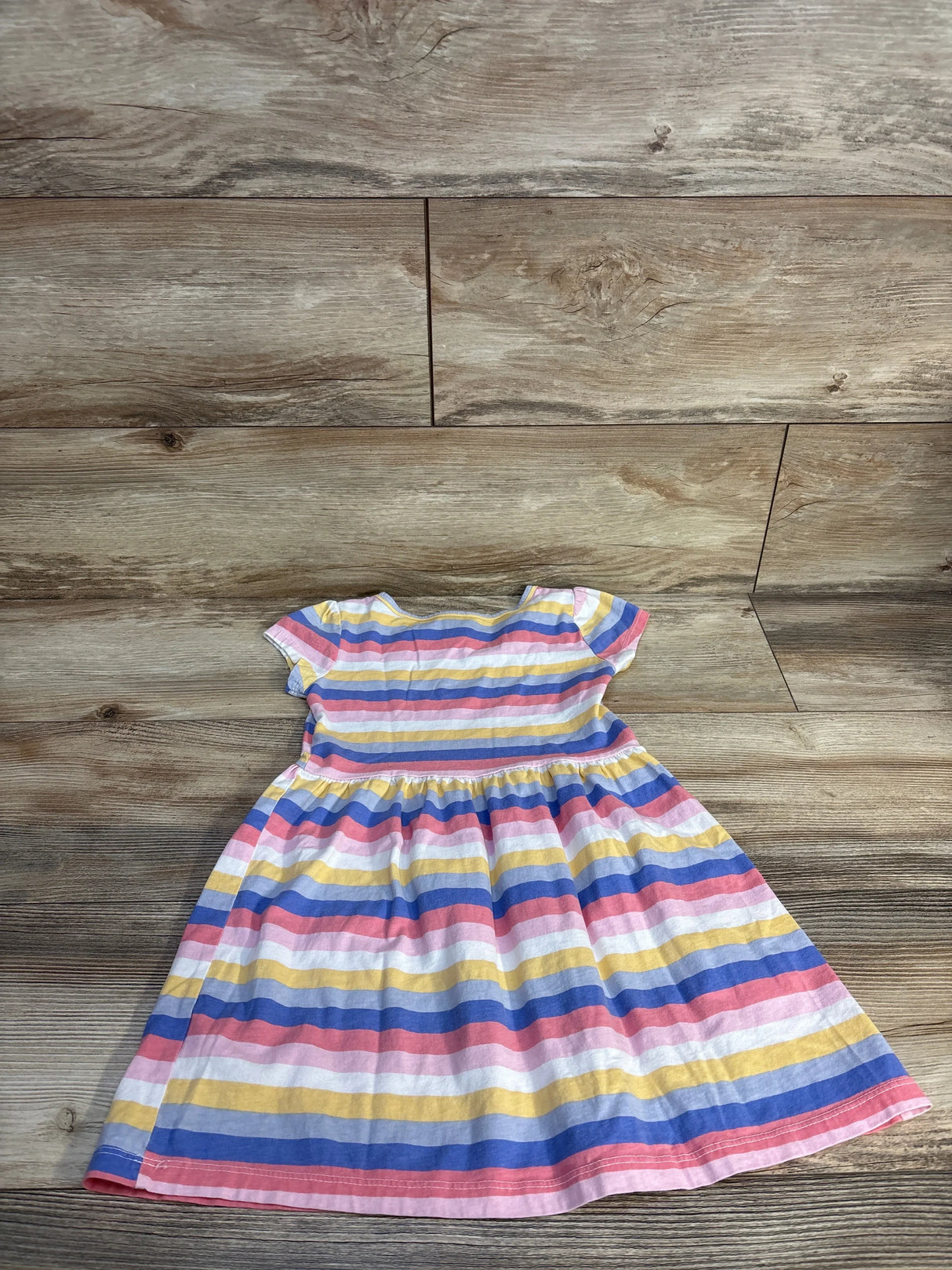 Flat-lay of Carter's girls' pink striped short-sleeve dress with gathered waist on wood floor