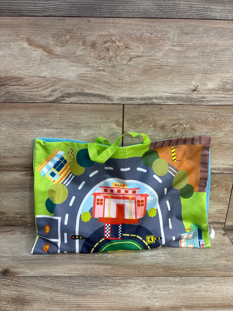 Front view of folded playmat showing printed road, bank and buildings with green carrying handles on wood background