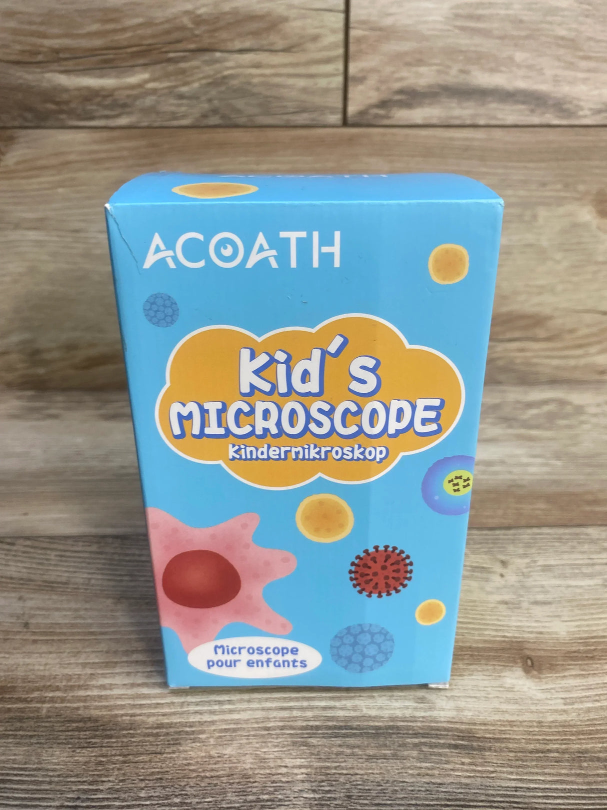 Kid's microscope science kit box with colorful cell illustrations on wood background