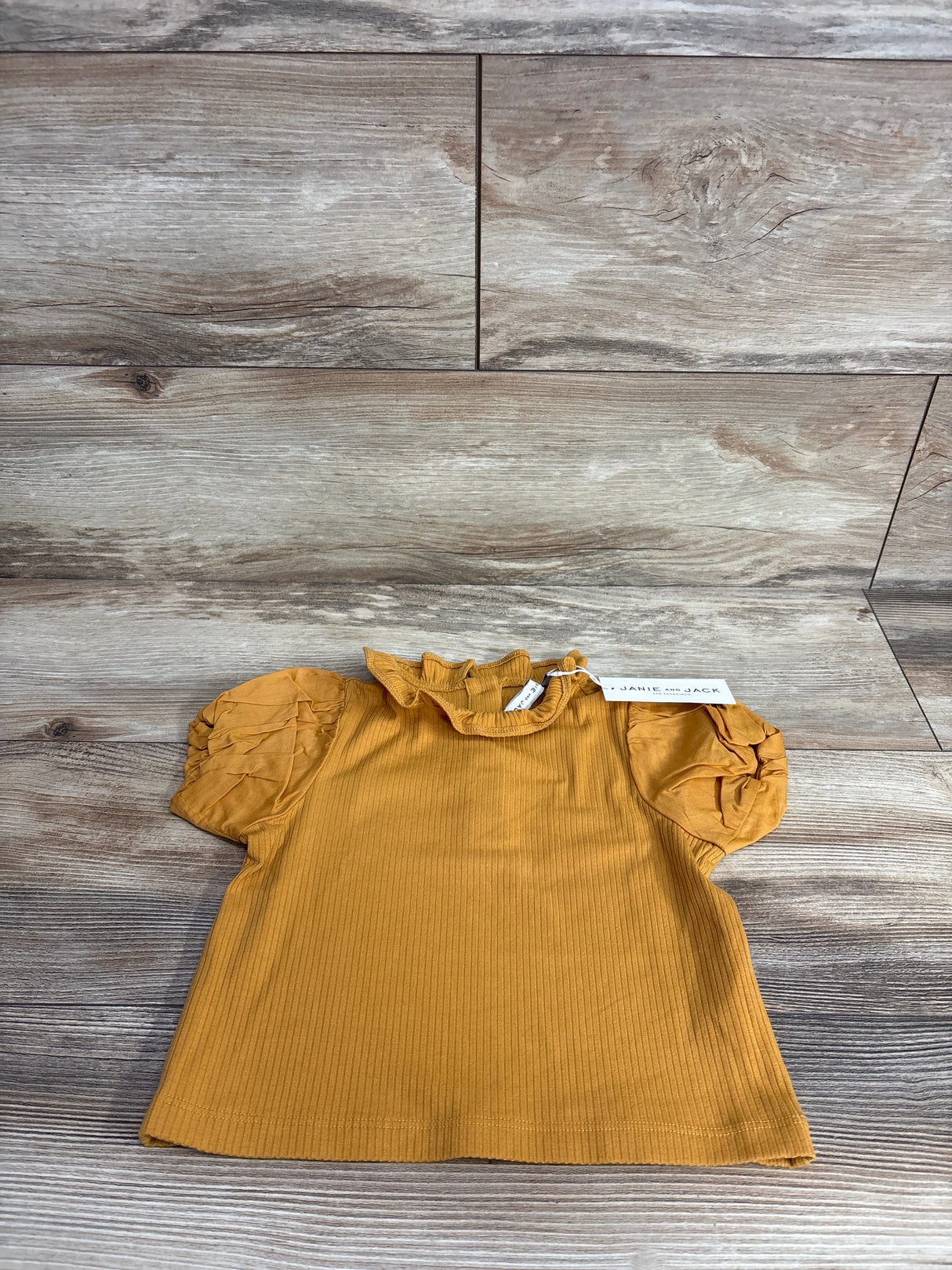 Mustard yellow ribbed toddler shirt with ruffled neck and puff sleeves on wooden floor