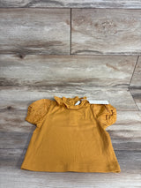 Mustard yellow ribbed toddler shirt with ruffled neck and puff sleeves on wooden floor