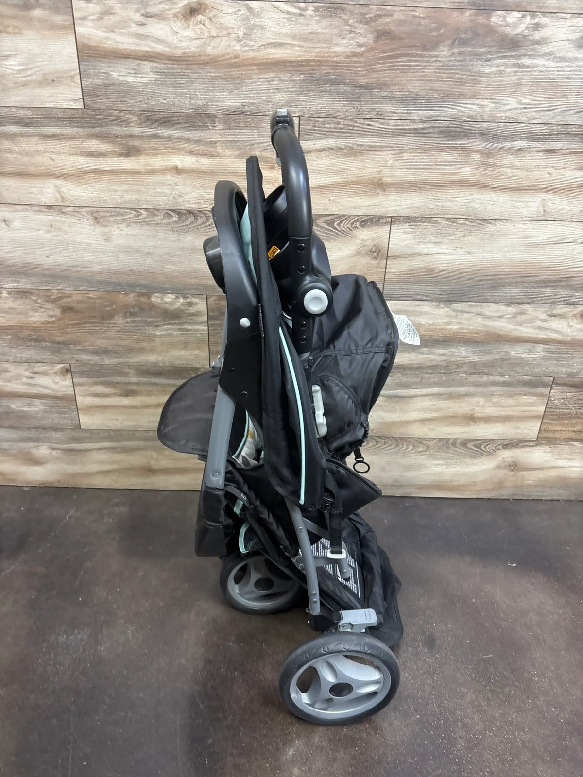 Side view of Baby Trend EZ Ride Stroller in Doodle Dots showcasing folded frame and wheels on a wood-look floor