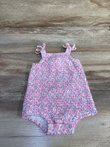 Flat lay of pink smocked bubble romper with tie straps, featuring smocking and elastic leg openings on wood background