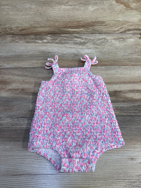 Flat lay of pink smocked bubble romper with tie straps, featuring smocking and elastic leg openings on wood background