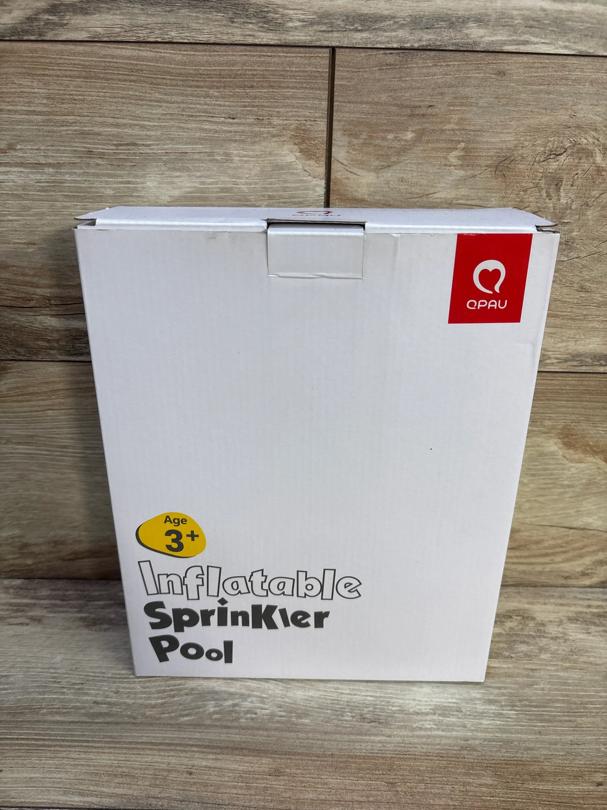 Front view of QPAU Pink Elephant box reading Inflatable Sprinkler Pool with QPAU logo and Age 3+ label on wood background
