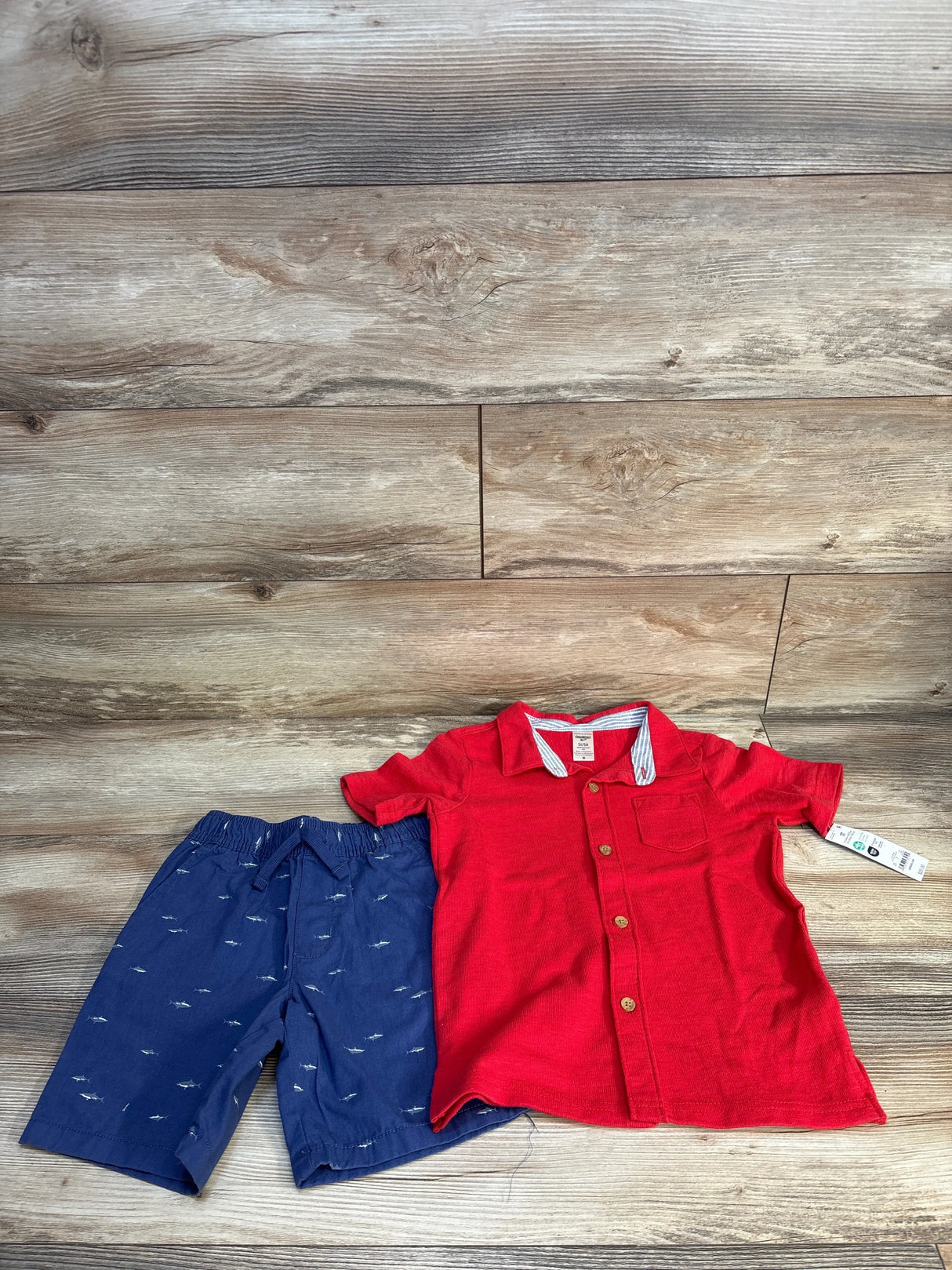 Red button-down shirt and navy shark-print shorts for toddler boys, laid on wood floor