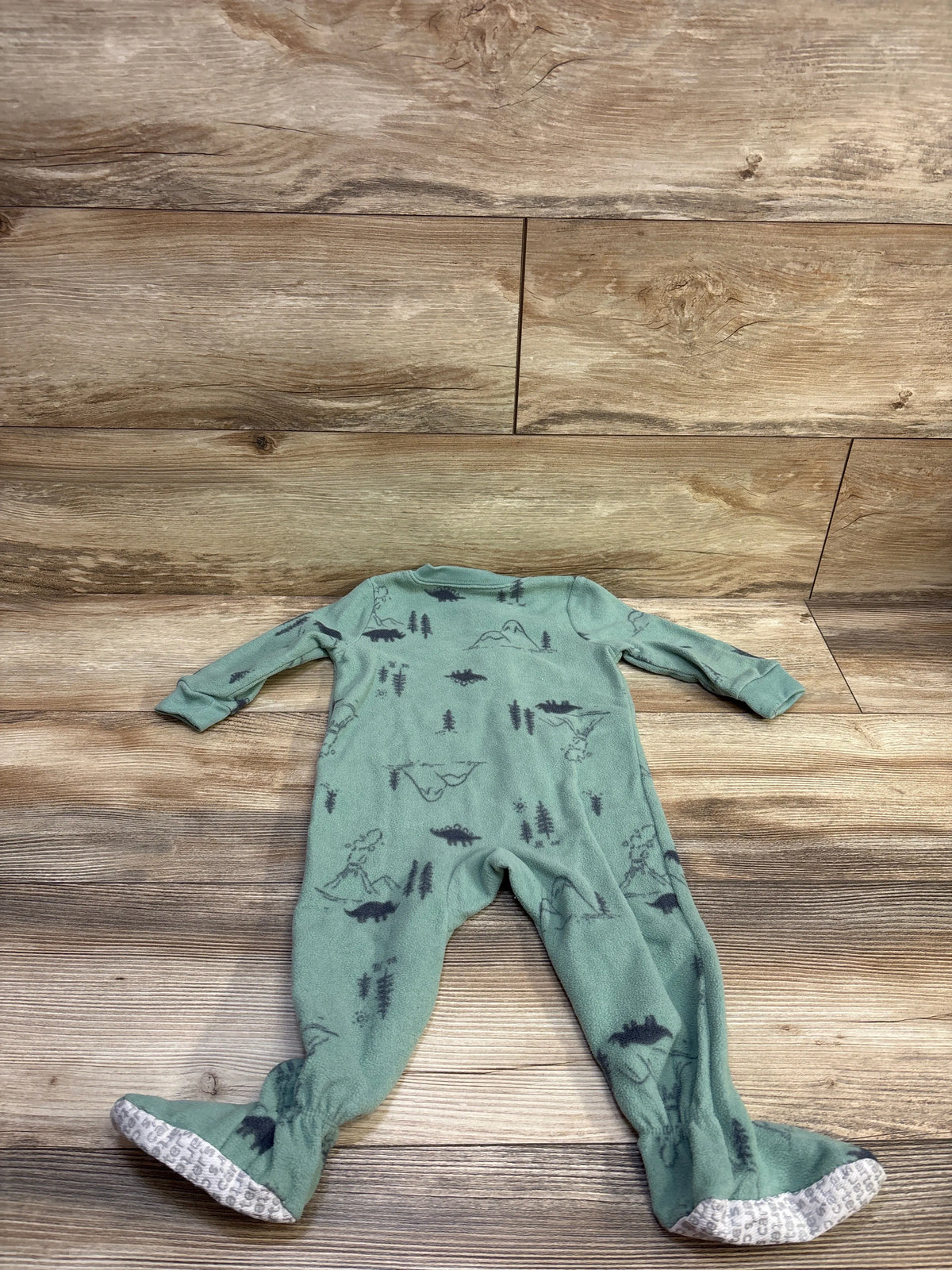 Front view of Just One You green blanket sleeper in size 12m showcasing dinosaur print and covered feet on wood background