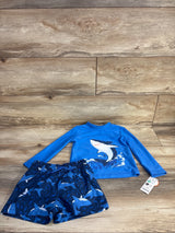 Flat lay of blue 2-piece shark rash guard set (2T) showing top with shark graphic and swim shorts on wood floor