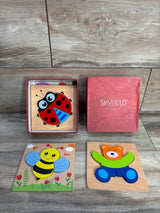 Top-down view of Skyfield 4 pack wooden animal puzzles showing colorful ladybug, bee, and bear pieces next to a red box on wood surface
