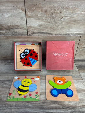 Top-down view of Skyfield 4 pack wooden animal puzzles showing colorful ladybug, bee, and bear pieces next to a red box on wood surface